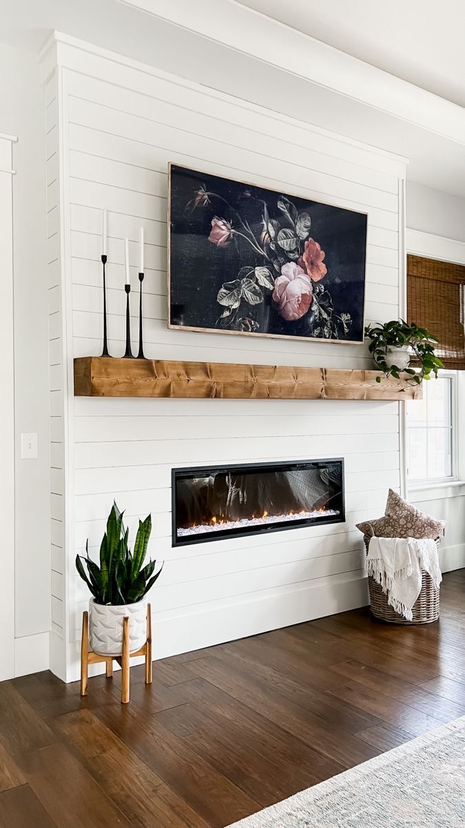 Fireplace with TV above, wooden mantel, and decorative plants in a white-walled room.