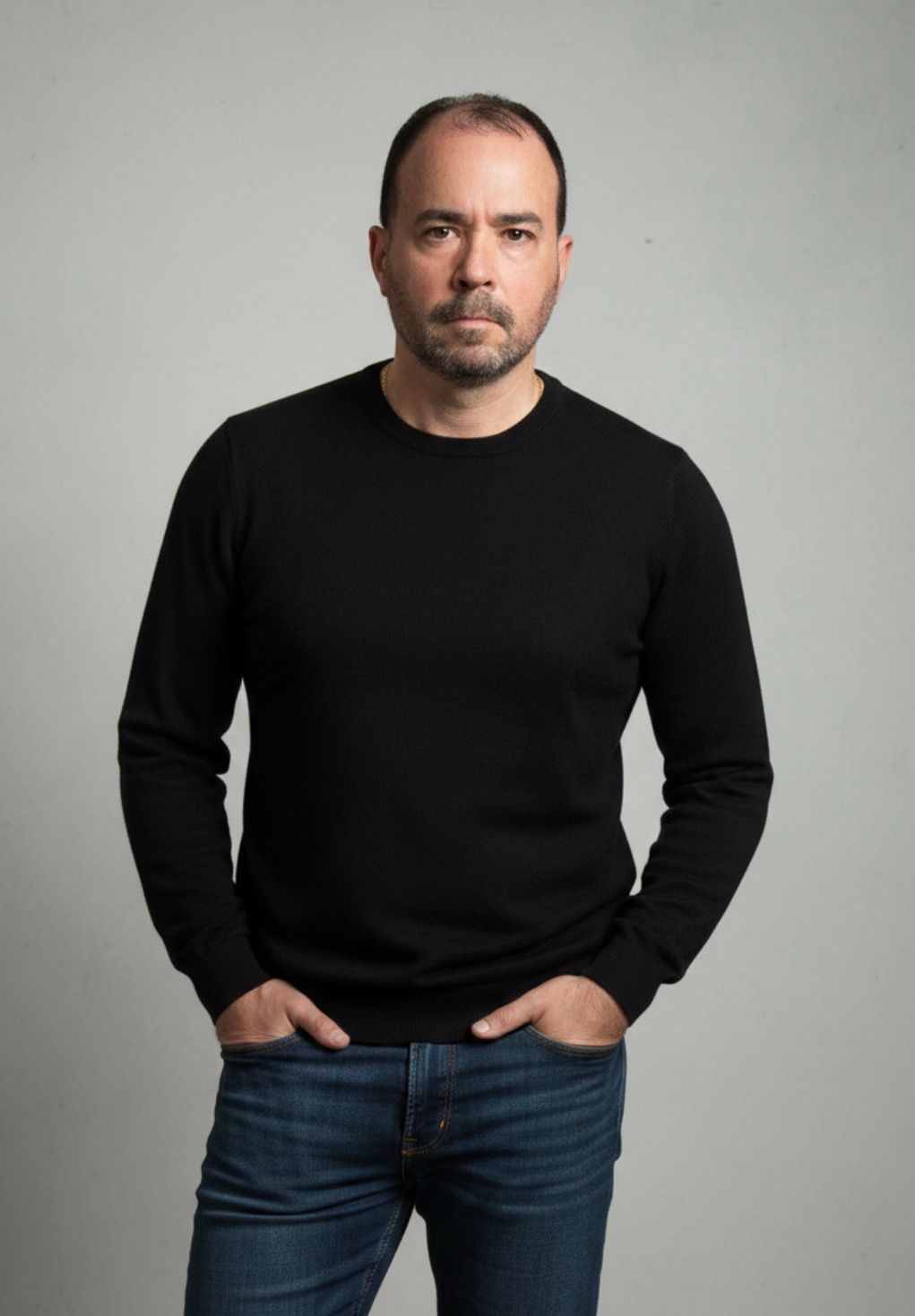 Man in a navy suit and glasses smiles for the camera. White background.