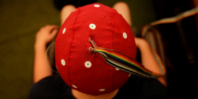 Person wearing a red cap with white dots, wires extending from the back.