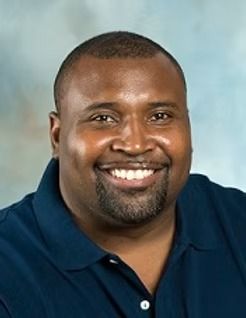 Man with short dark hair, wearing a blue polo, smiling.