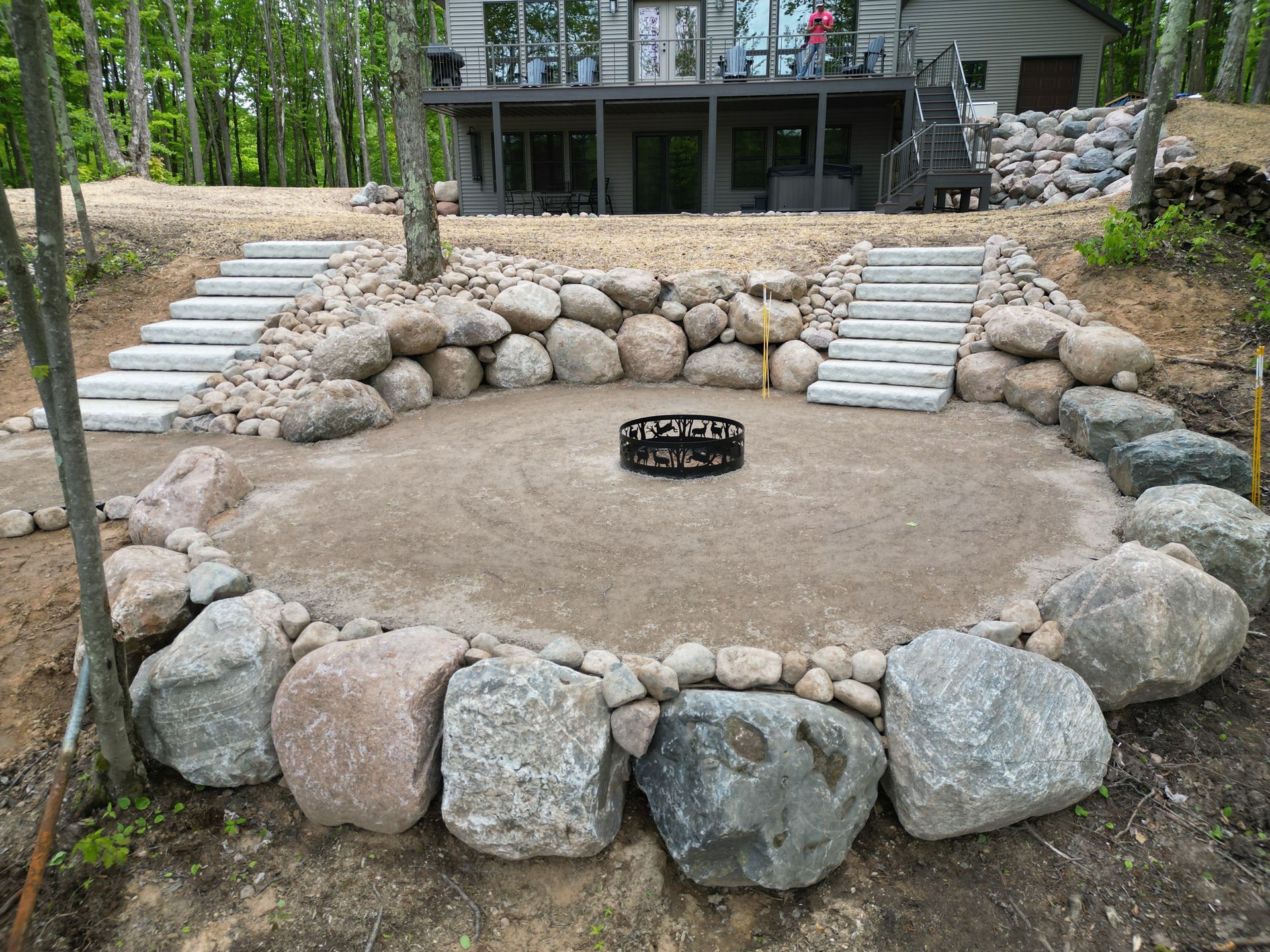 Circular fire pit with stone border, stairs, and a house in the background.