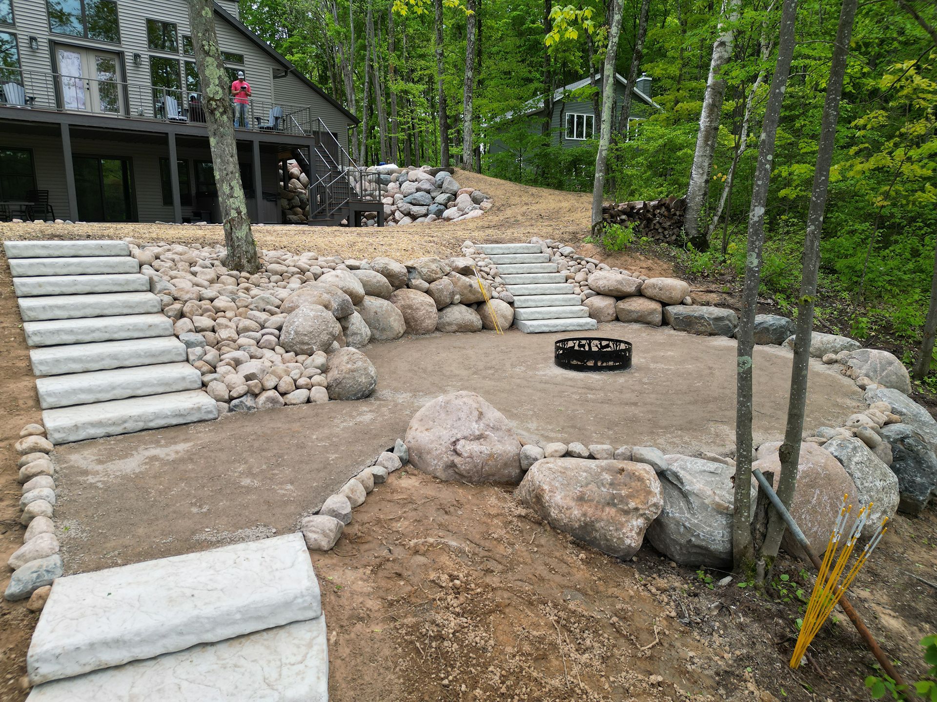 Stone steps and a fire pit area in a wooded setting, with a house in the background.