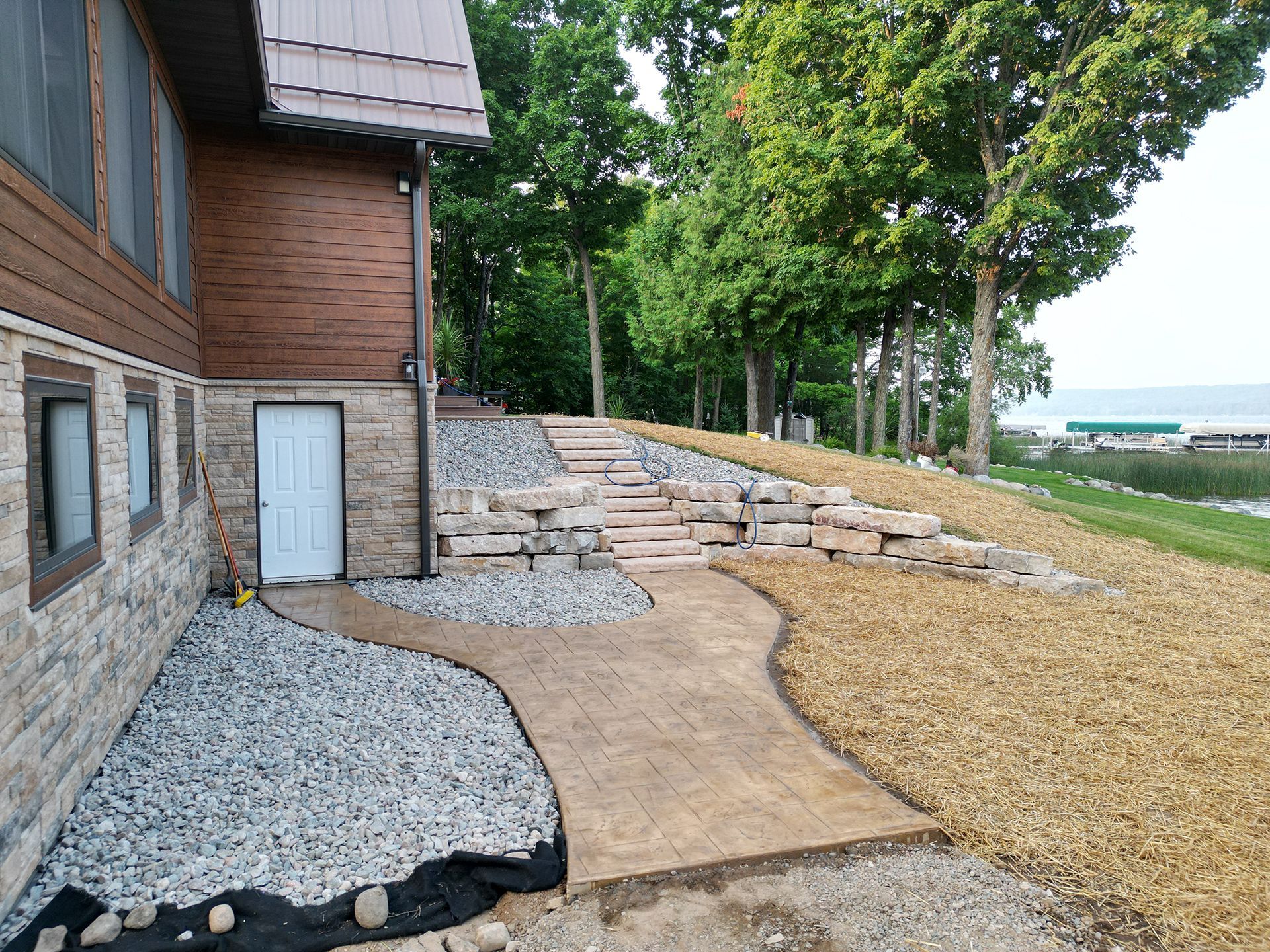 Exterior of a house with stone siding, a concrete pathway, stairs, and landscaping leading to a waterfront.