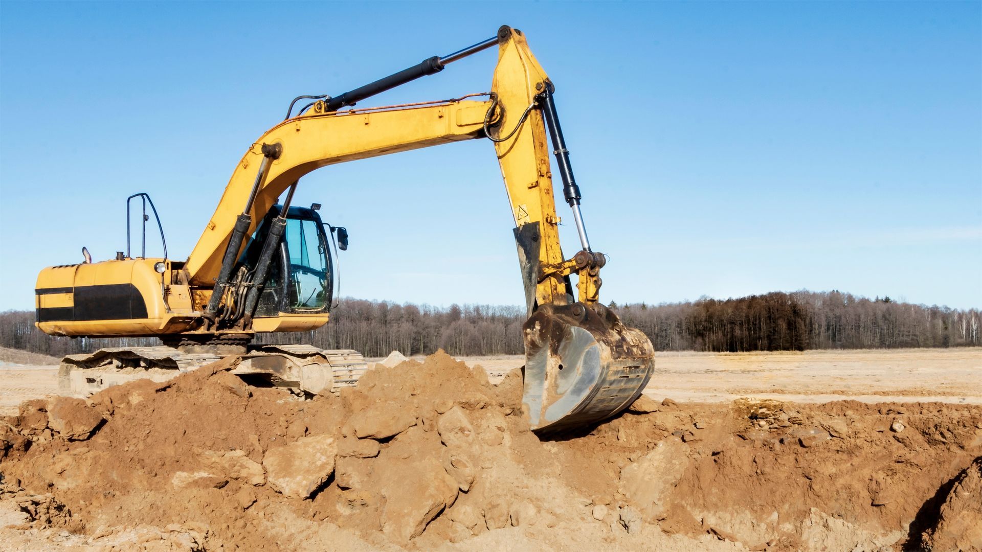 Yellow excavator digging into a pile of dirt under a blue sky.
