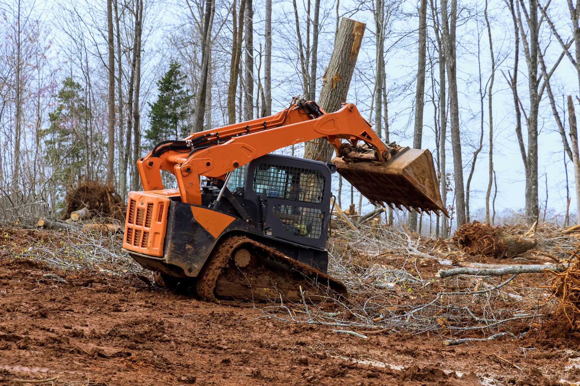 Person using a shovel to clear debris from a room under construction; wearing grey pants and orange gloves.