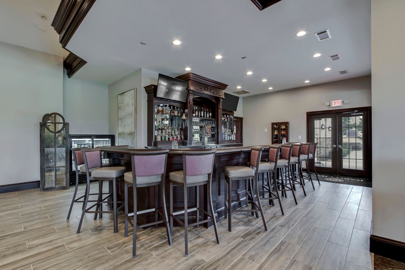 Dark wooden bar with bar stools, shelves of liquor, and a television.