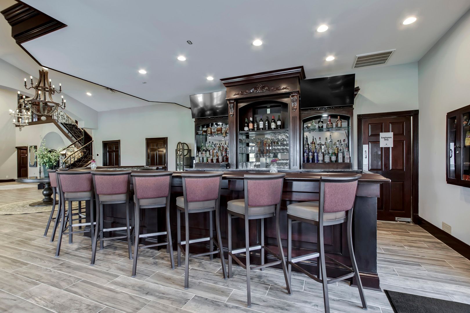 Bar with wooden facade, stocked liquor shelves, and tall maroon bar stools in a large room.
