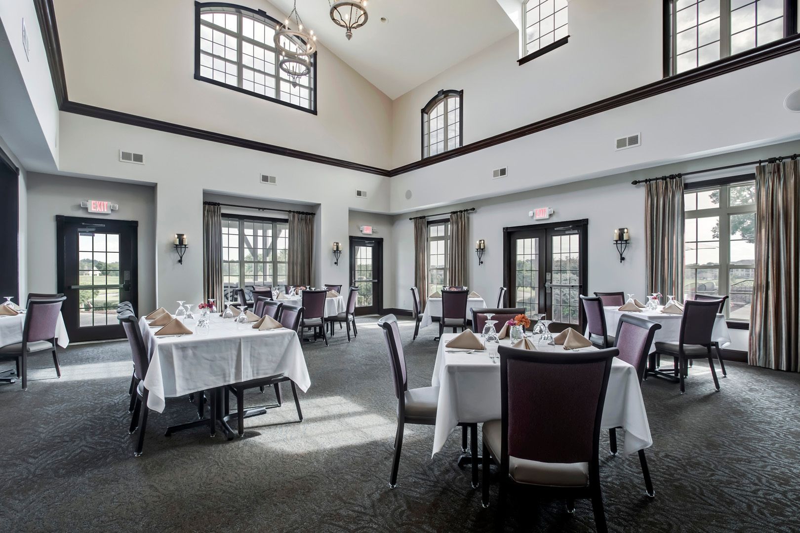 Elegant dining room with tables set for a meal. Windows and doors provide natural light.