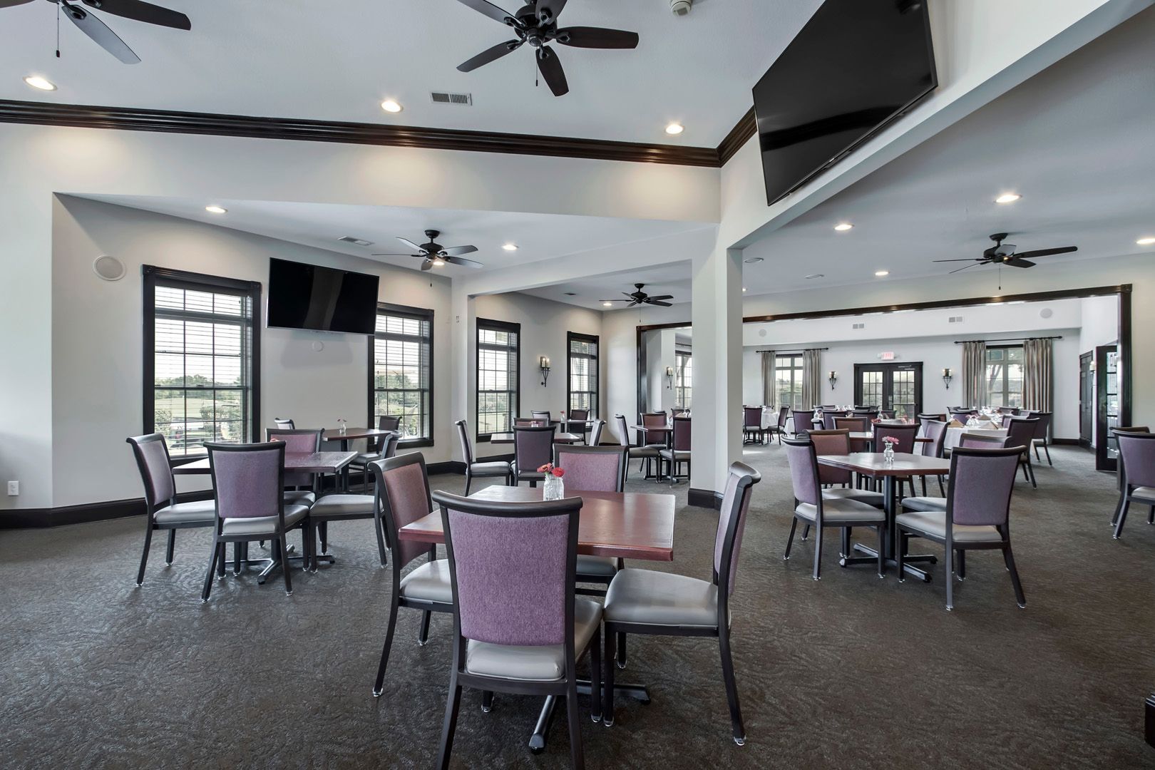 Restaurant dining area with tables, chairs, windows, ceiling fans, and a television.