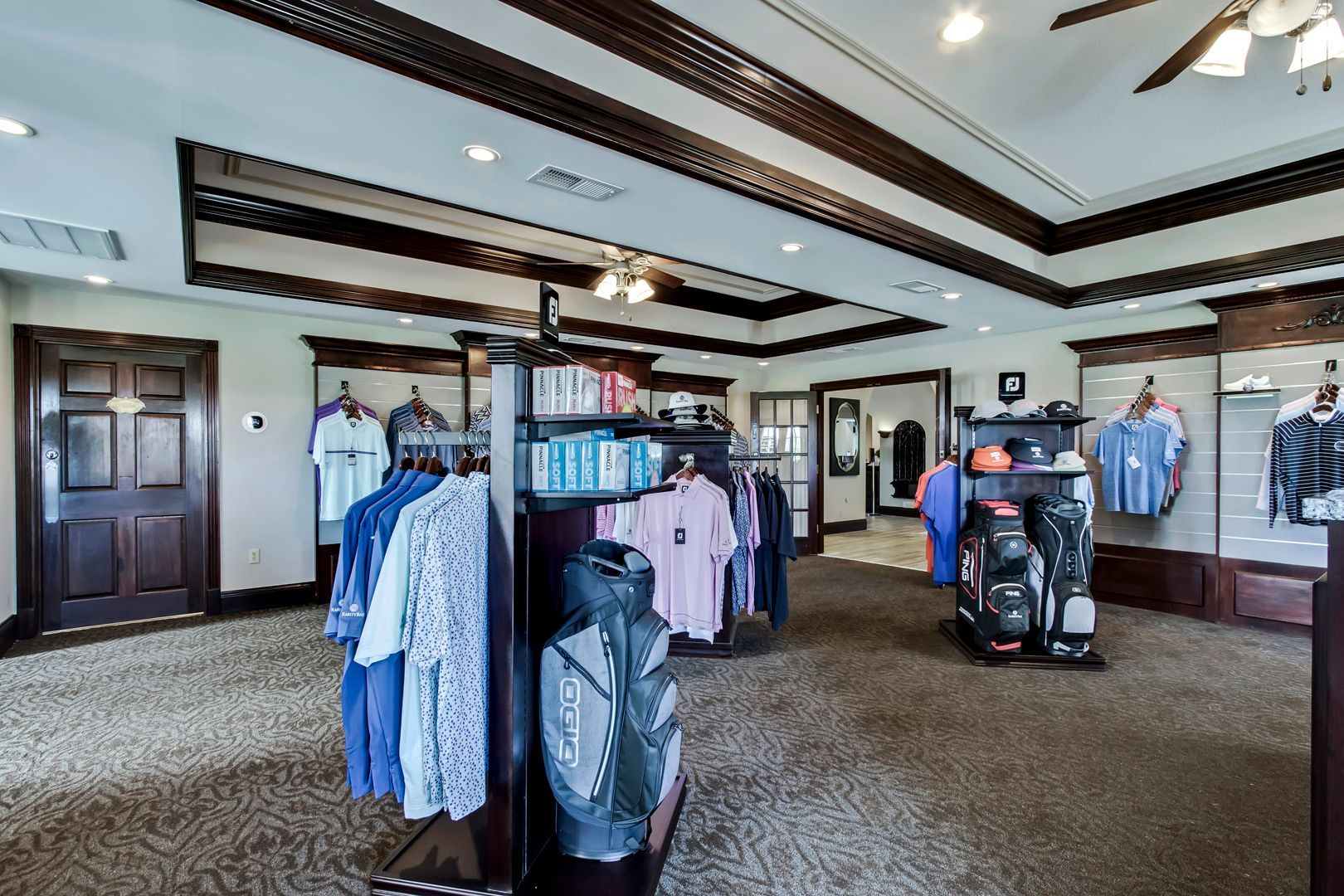Golf shop interior with clothing racks, golf bags, and wooden ceiling beams.