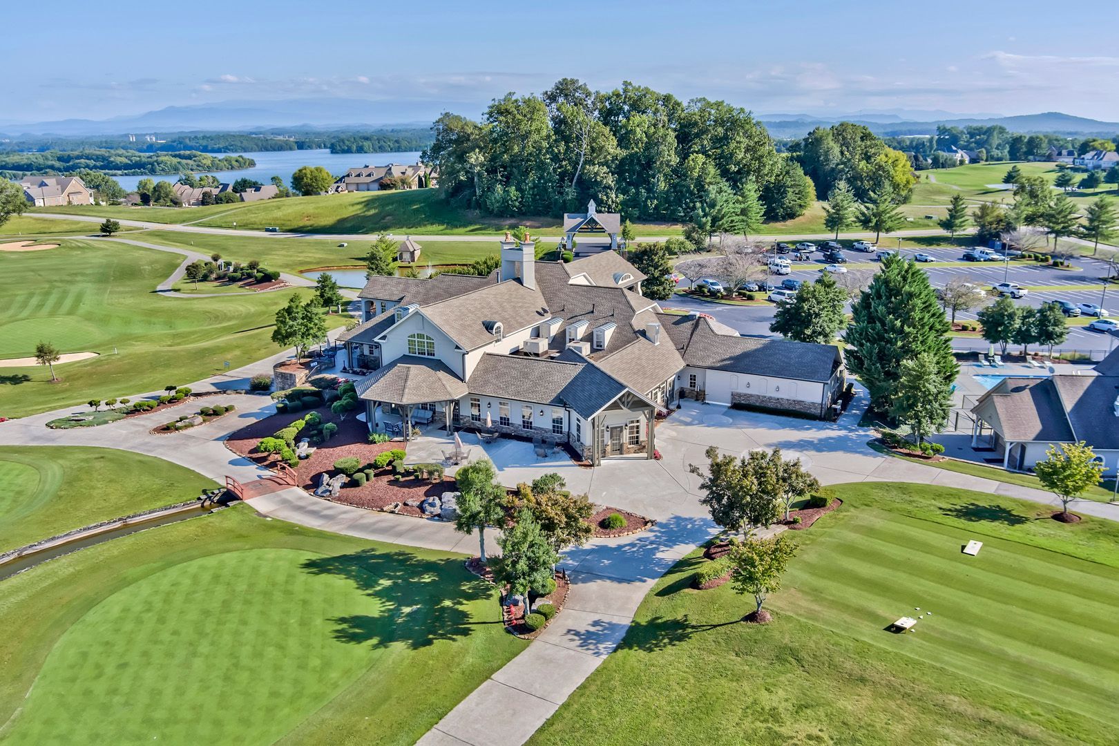 Aerial view of a clubhouse on a golf course with green grass, trees, and a lake in the background.