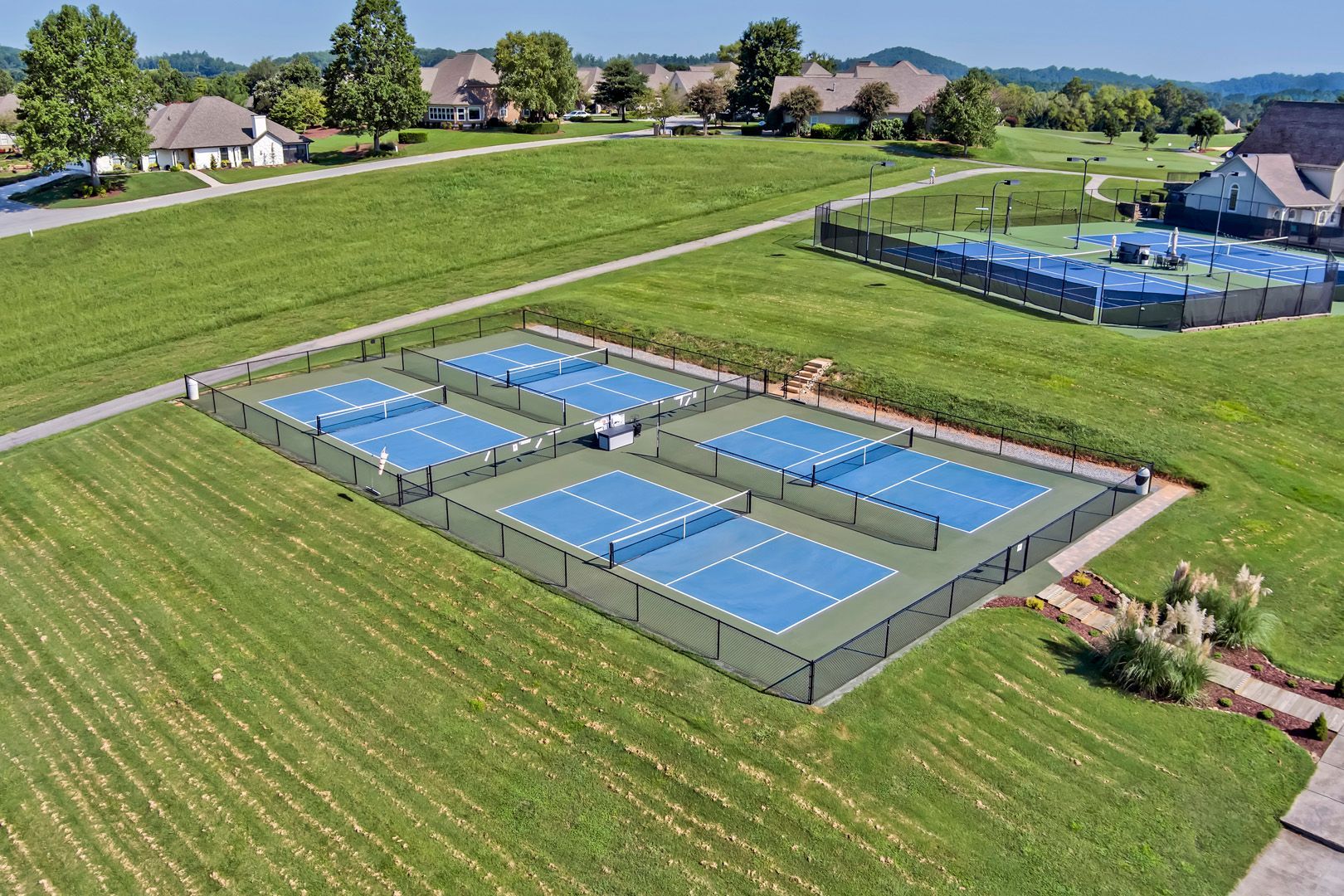 Tennis player in white shorts and visor swings racket on green court, shadow visible.