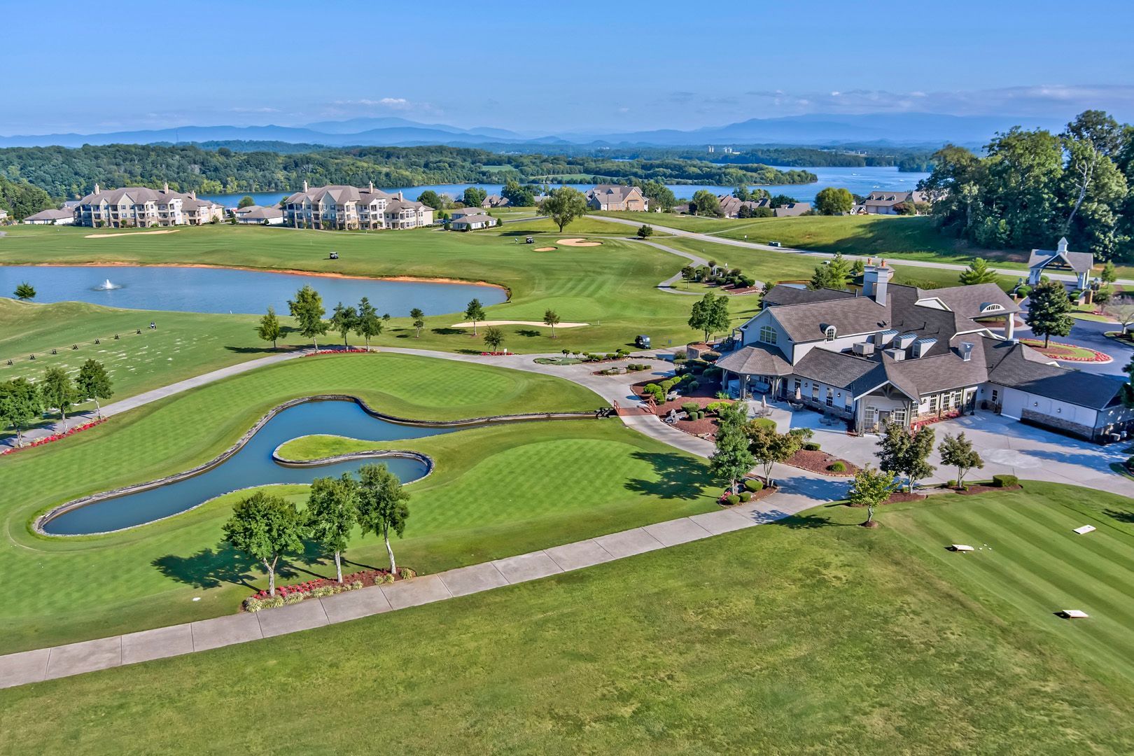 Golf course with clubhouse, lake, and distant mountains under a blue sky.
