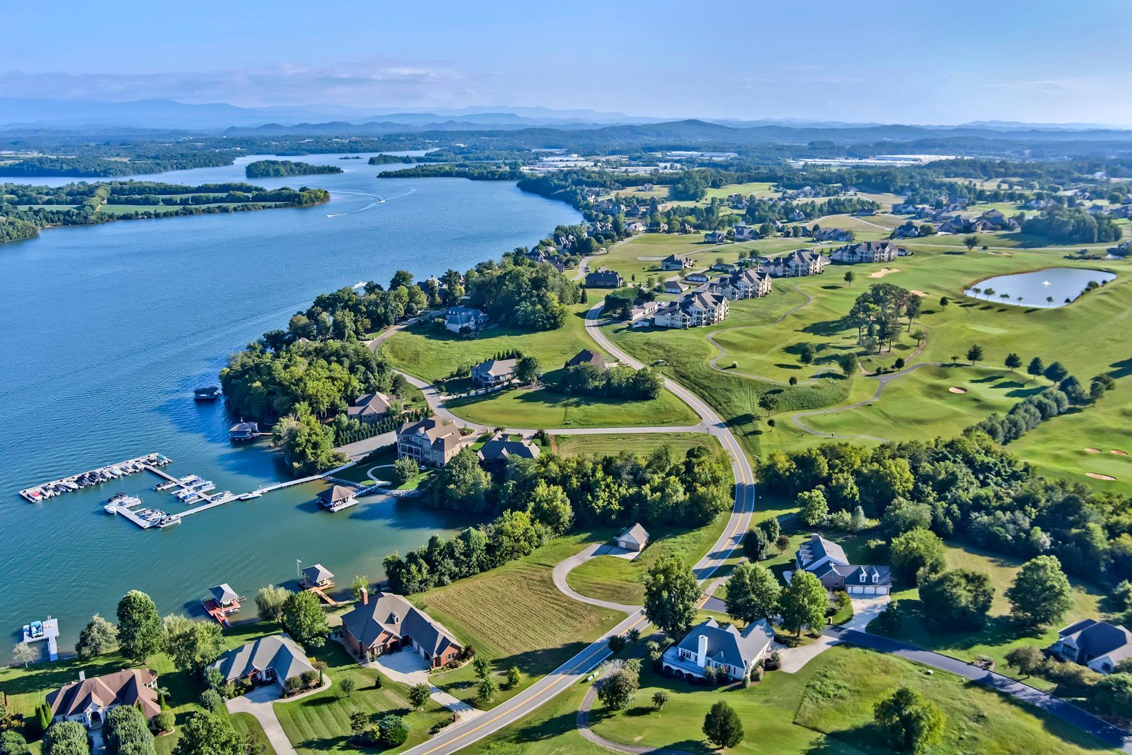 Aerial view of a lakefront community with homes, a marina, and green spaces under a blue sky.