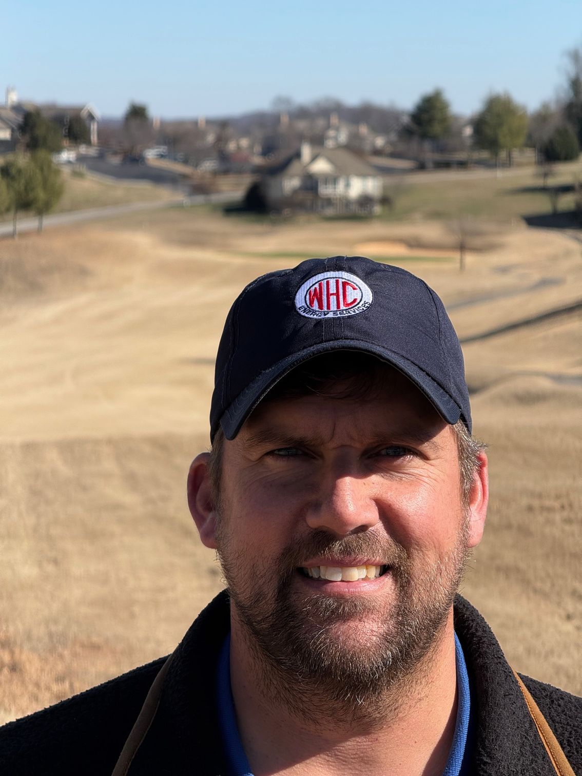 Tennis player in white shorts and visor swings racket on green court, shadow visible.