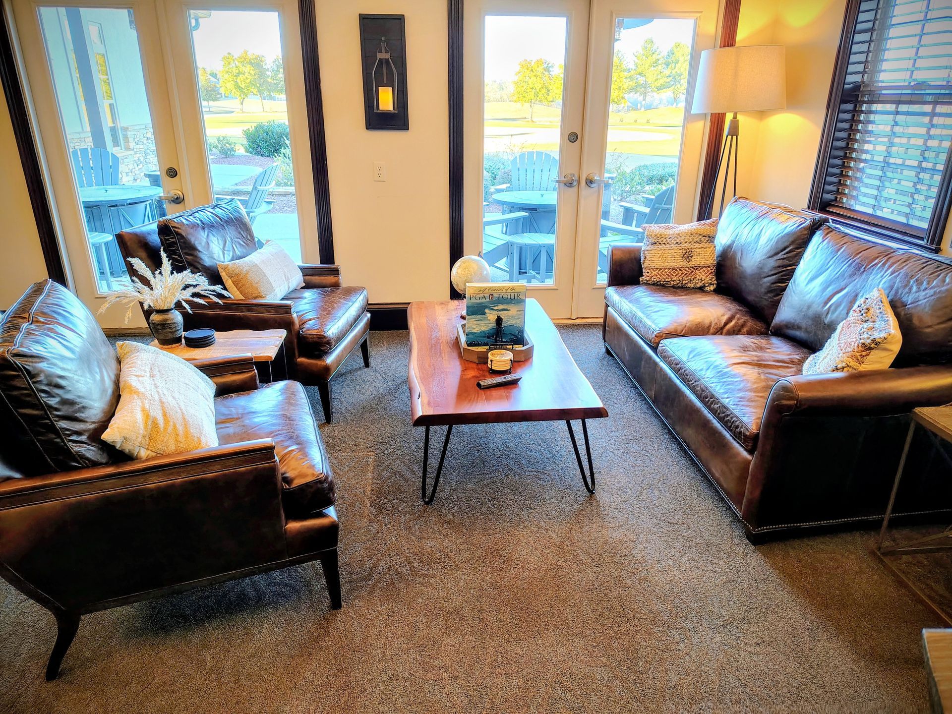 Living room with brown leather furniture, coffee table, and open doors to a view.