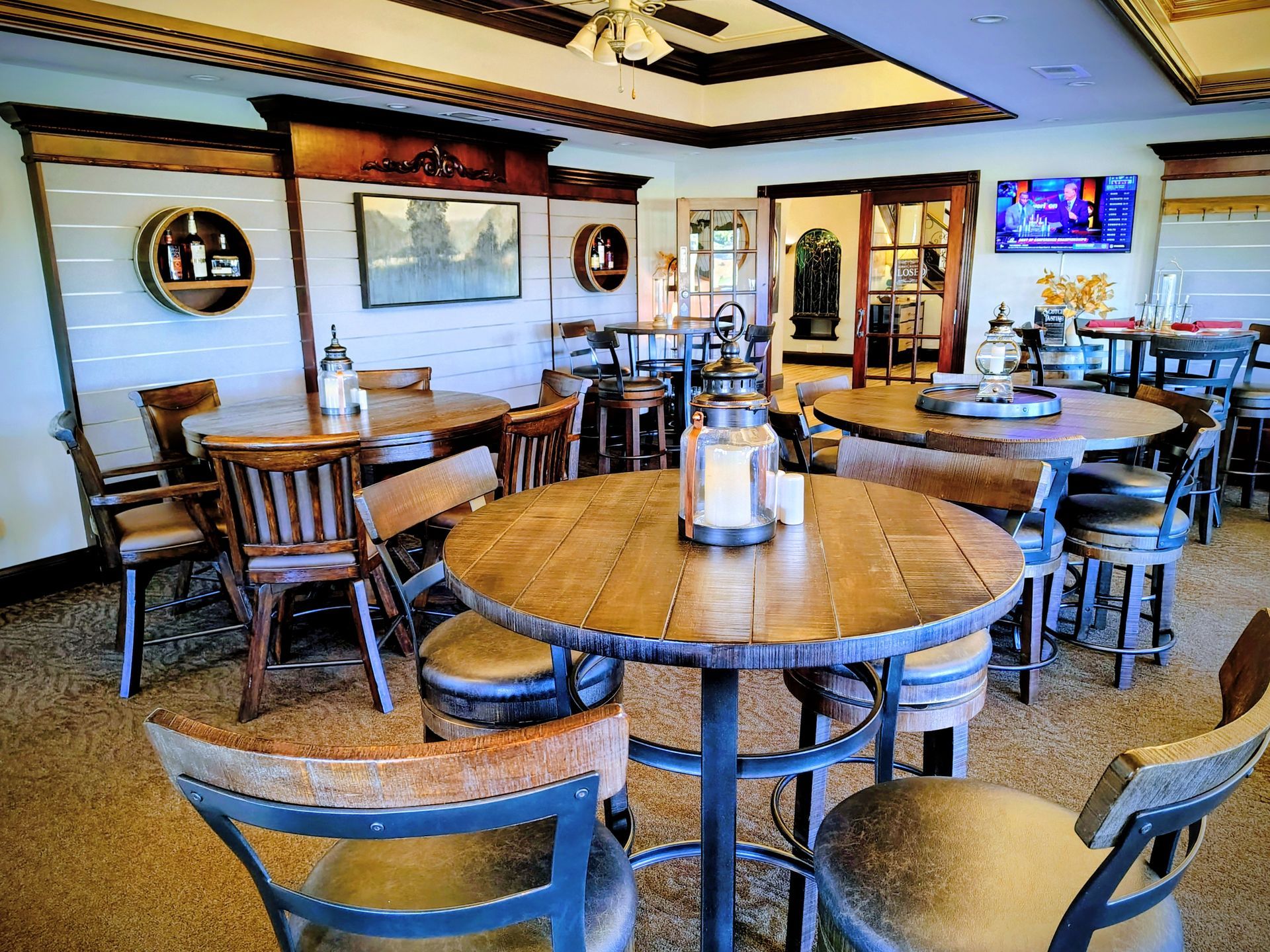 Restaurant interior with round wooden tables, bar stools, and a television.