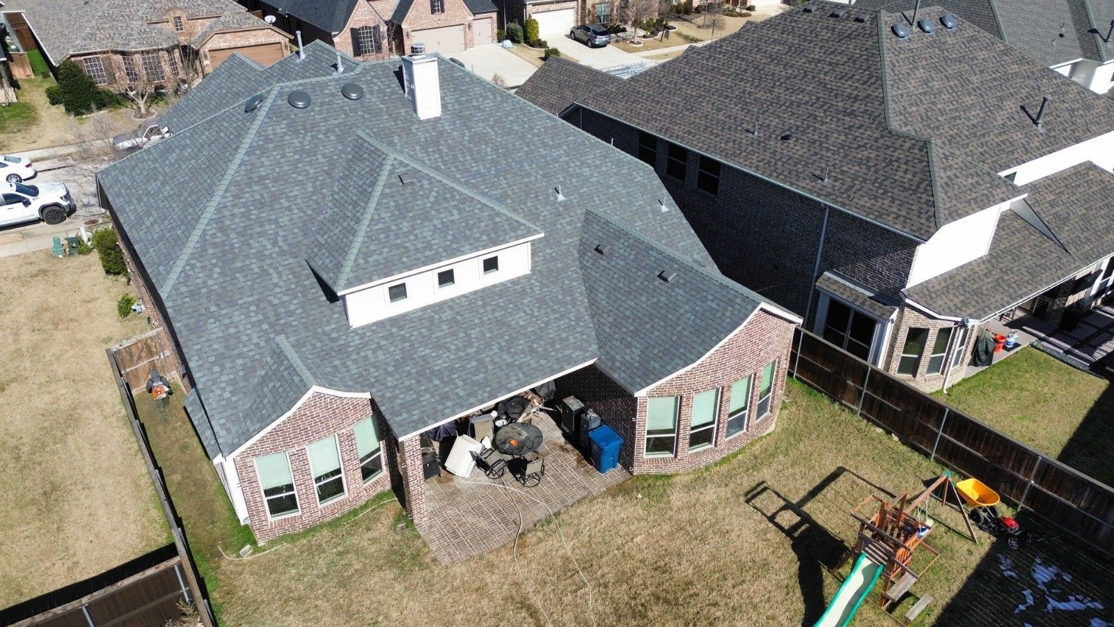 Aerial view of a brick and gray roof house with a patio and small playground in the backyard.