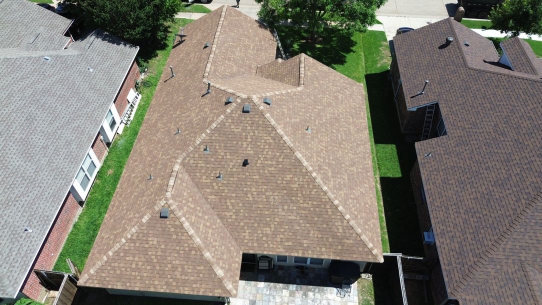 Brown roof of a house, aerial view. Adjacent to a gray roof and green grass yard.