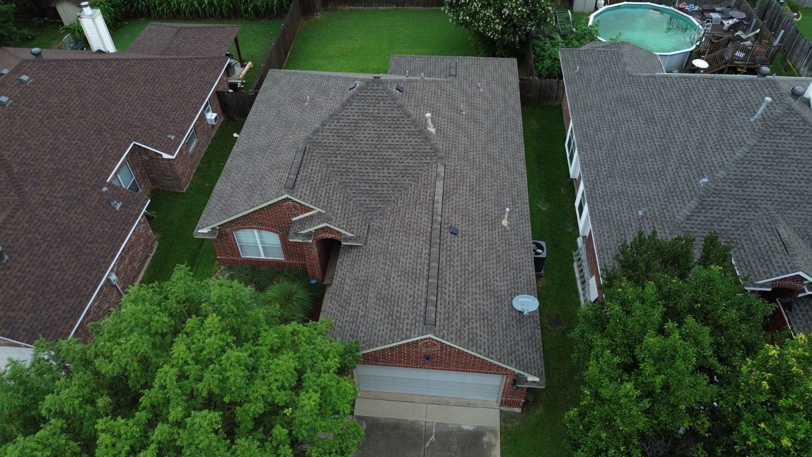 Aerial view of a brown-roofed brick house with a driveway, surrounded by green lawns and trees.