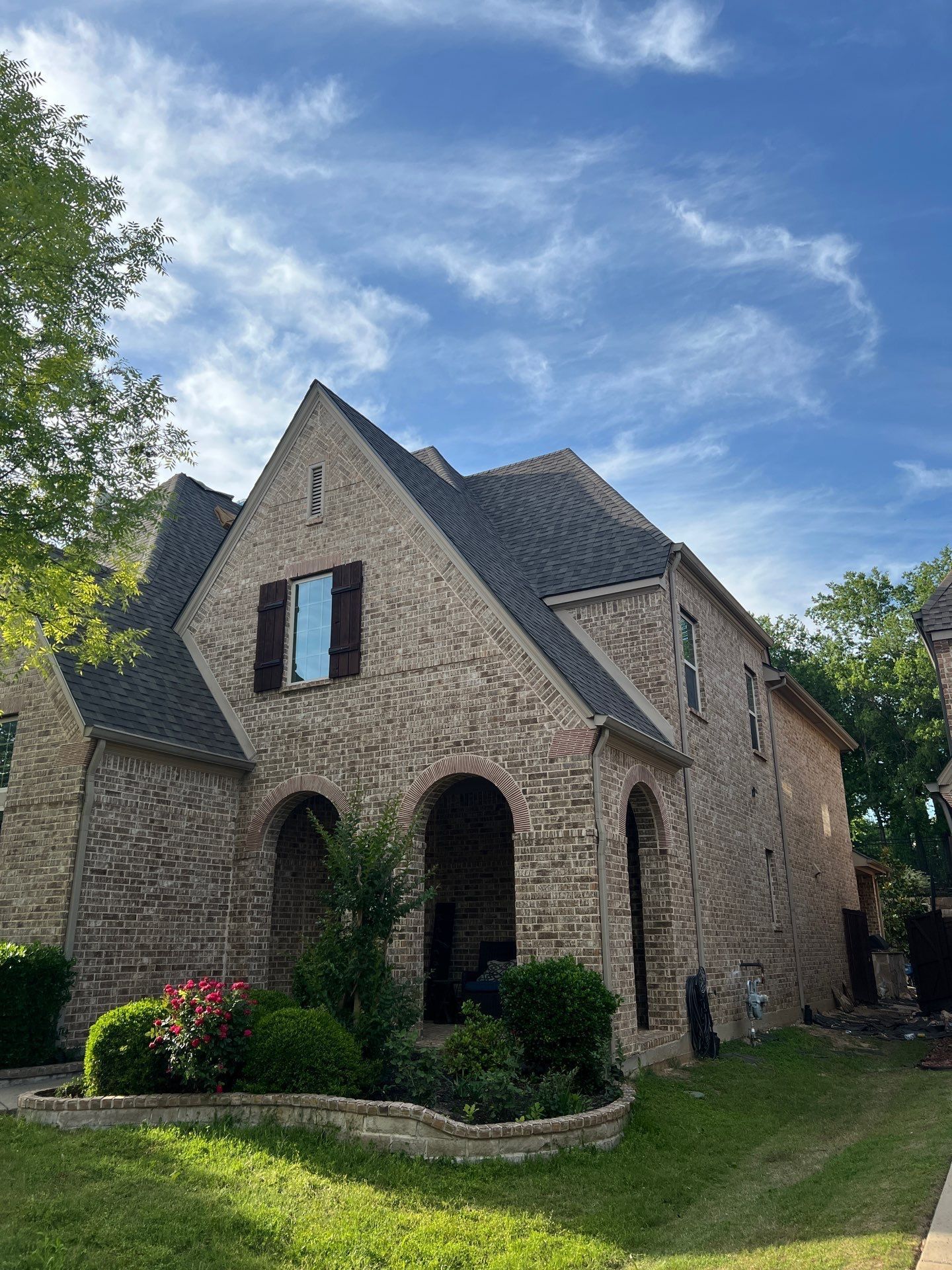 Brick house with arched entry, brown shutters, and dark roof under a blue sky.