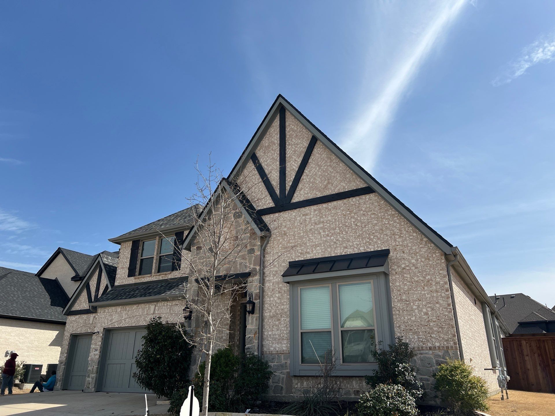 Two-story brick house with black trim against a blue sky, trees, and a garage.