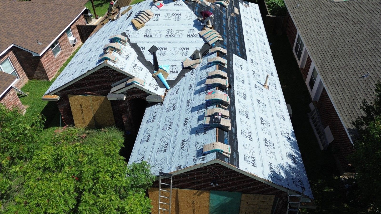 Roofers working on a residential roof, laying down roofing material. Aerial view, daytime.