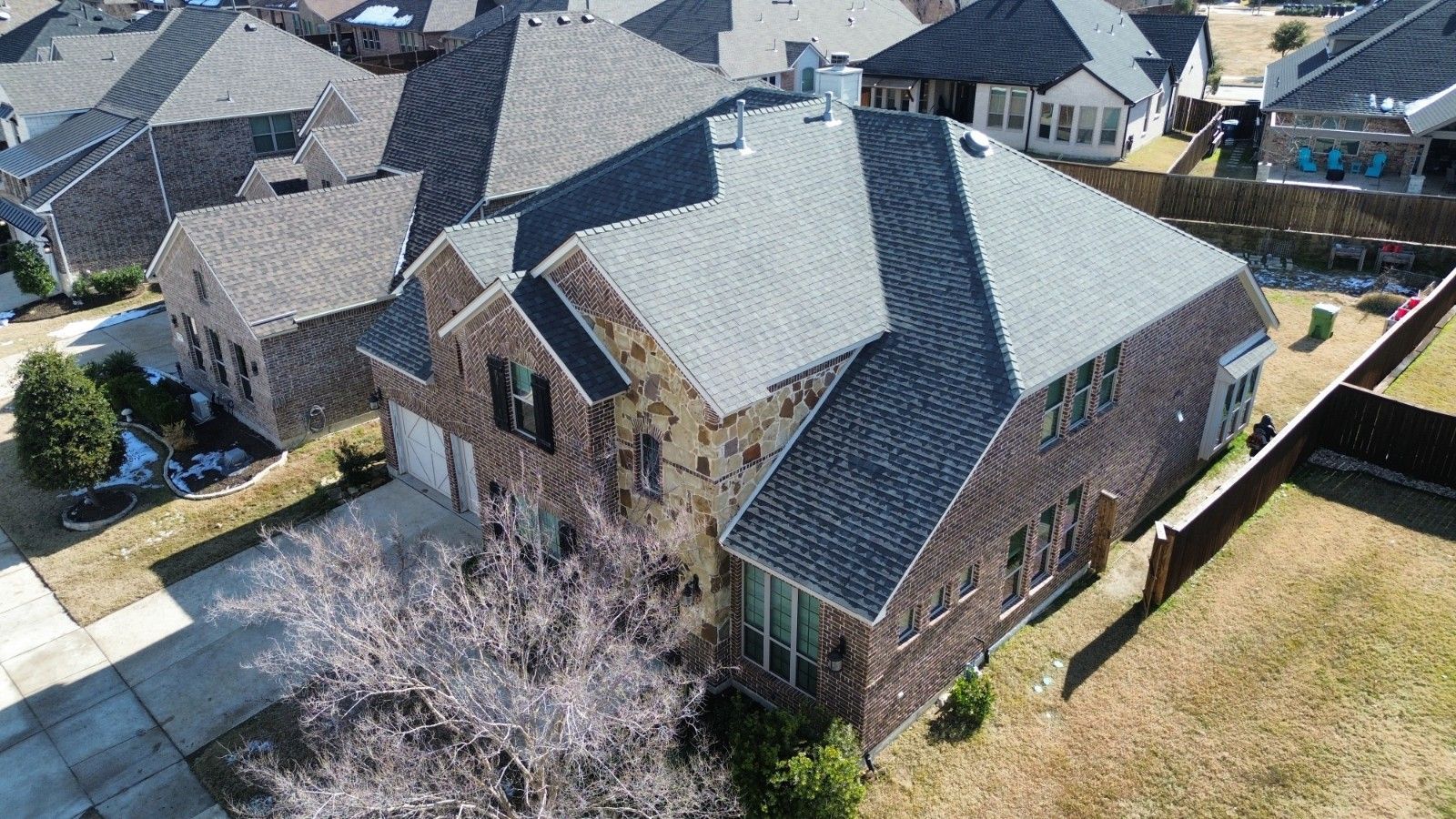 Aerial view of a two-story brick home with a gray shingle roof in a suburban neighborhood.