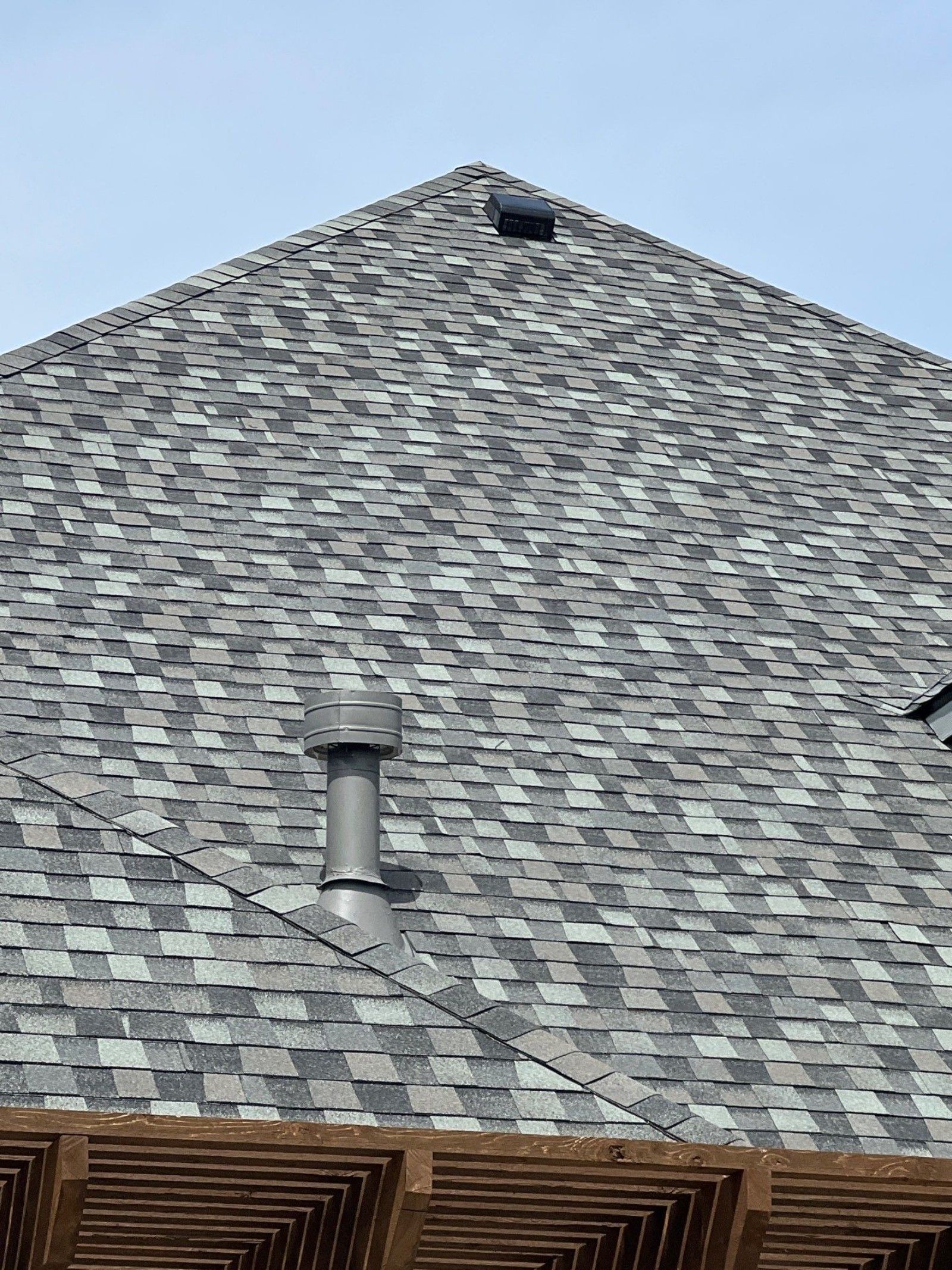 Grey shingle roof with a chimney, viewed from below with blue sky in the background.
