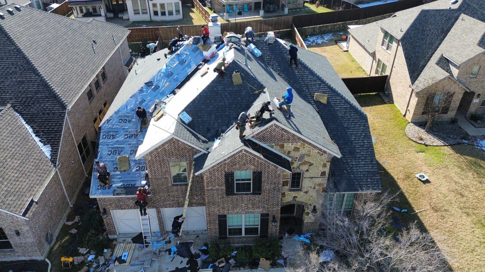 Roofers working on a two-story house with a partially replaced roof; sunny day.