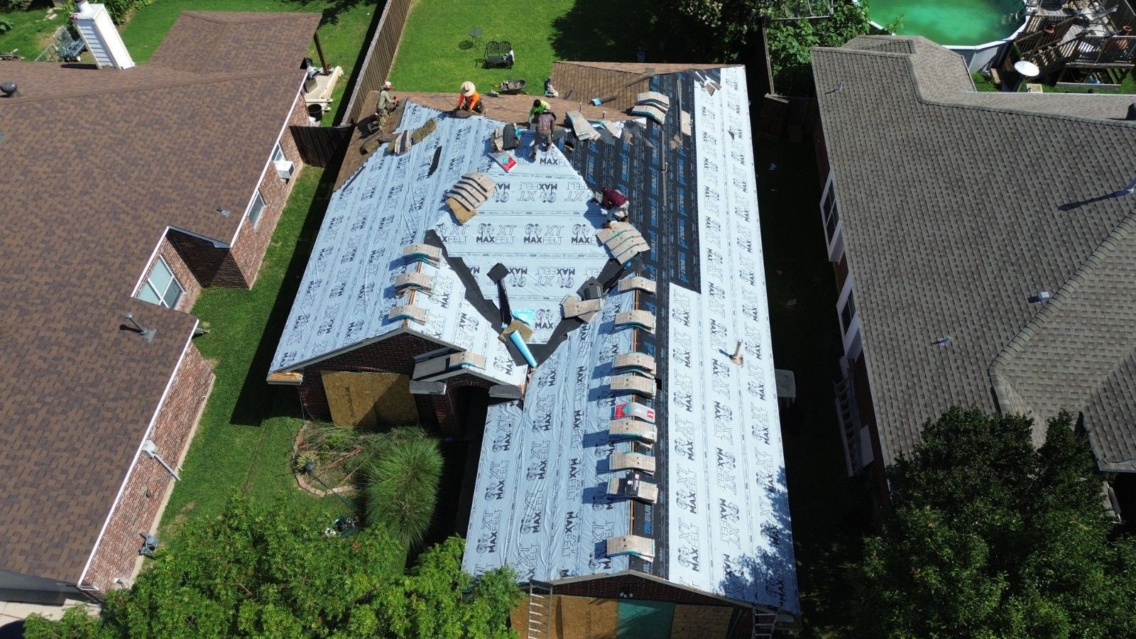 Aerial view of roof replacement in progress; workers, materials, and partially shingled roof.