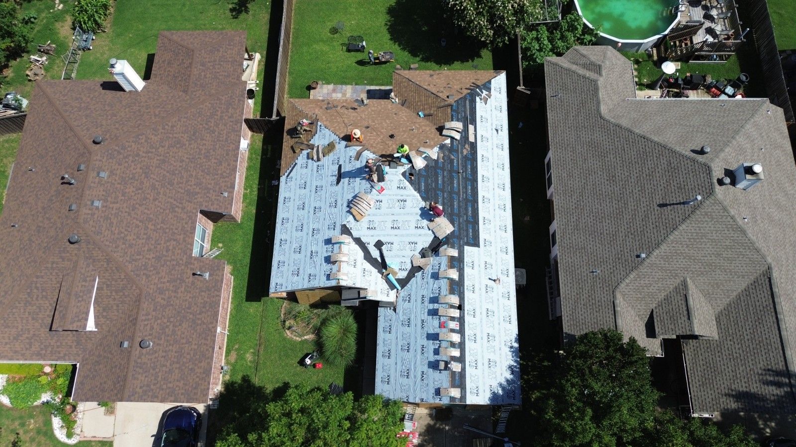 Aerial view of a roof being worked on by several people. Brown and gray roofing materials are visible.