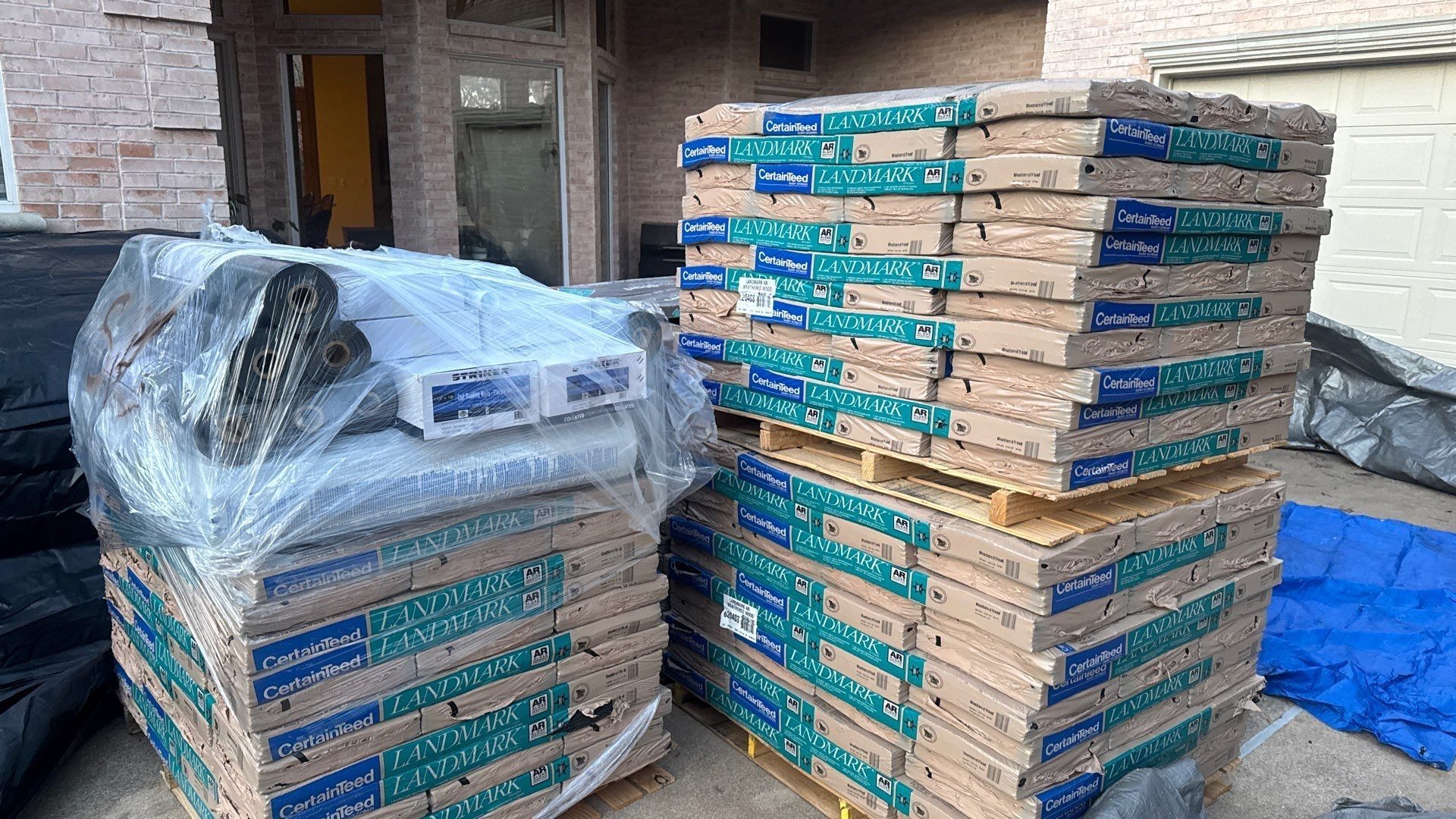 Pallets of flooring materials wrapped in plastic, beside a building.
