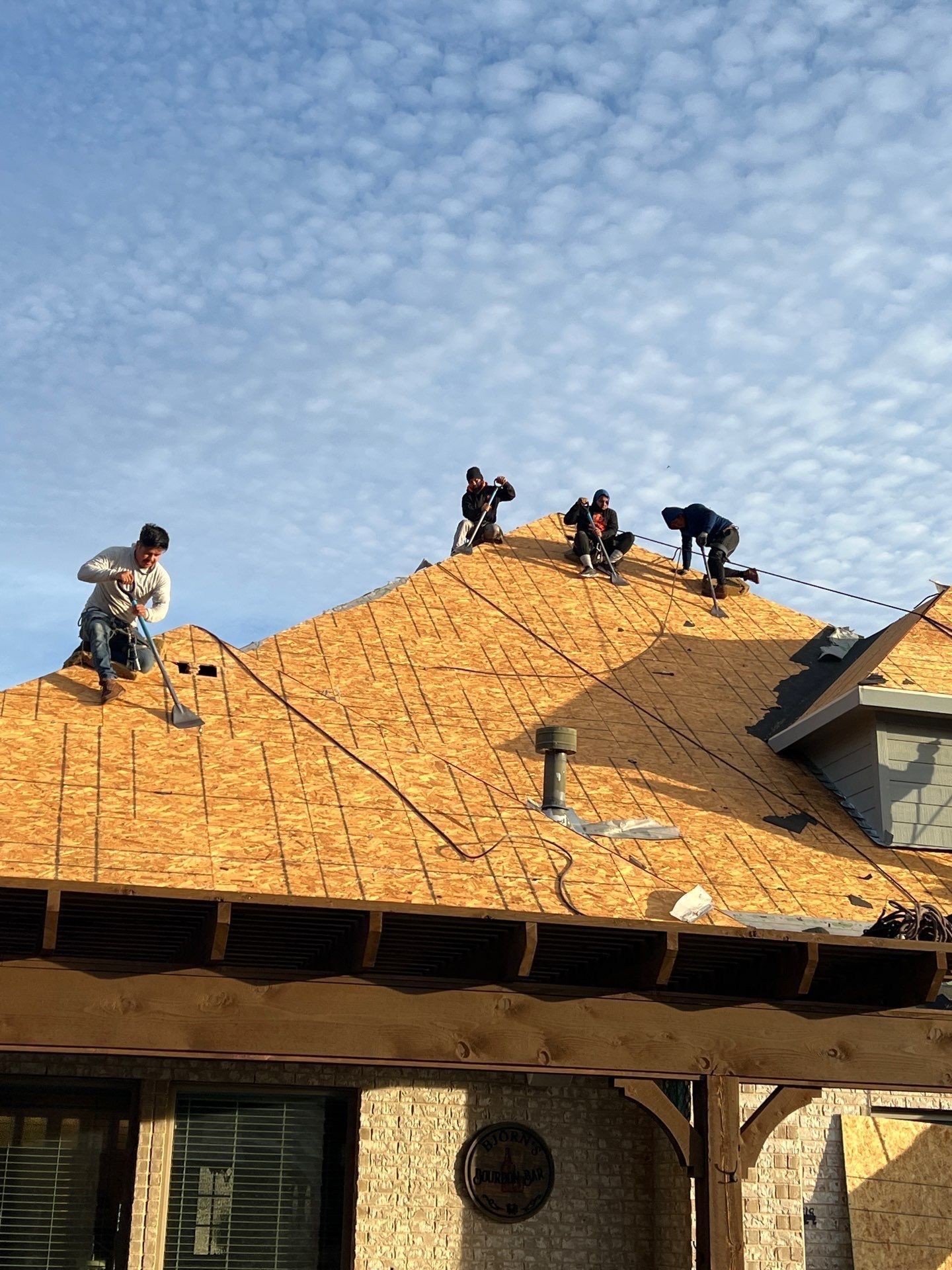 Roofers working on a house roof under a cloudy blue sky.