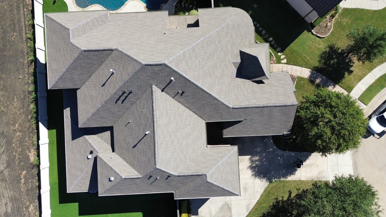 Aerial view of a gray-roofed house with a complex roofline, surrounded by green lawns and a driveway.
