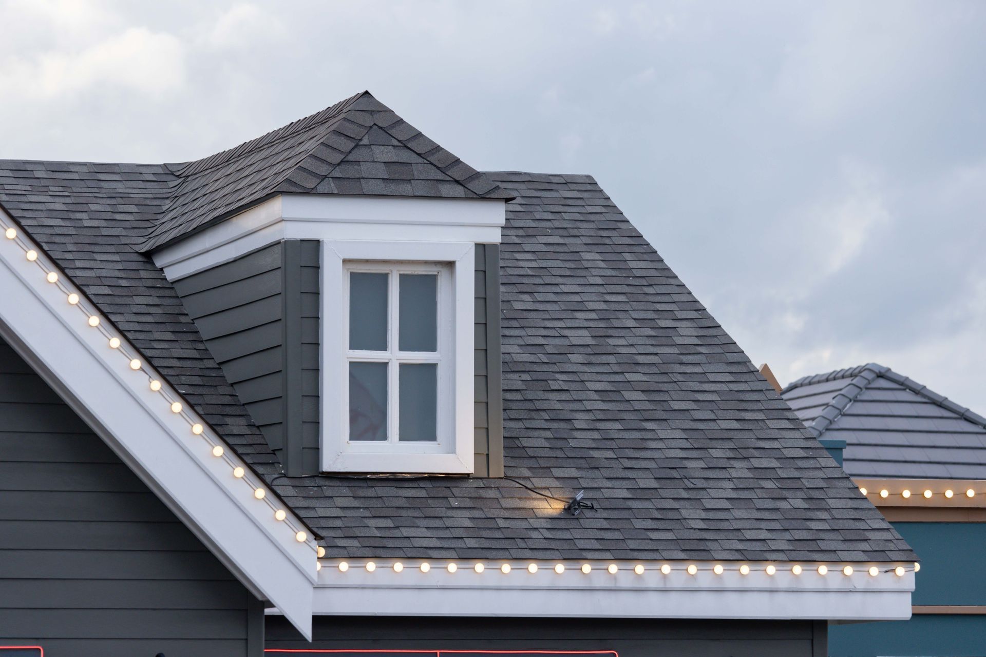 Grey roof with a white-framed dormer window and white trim. String lights adorn the eaves.