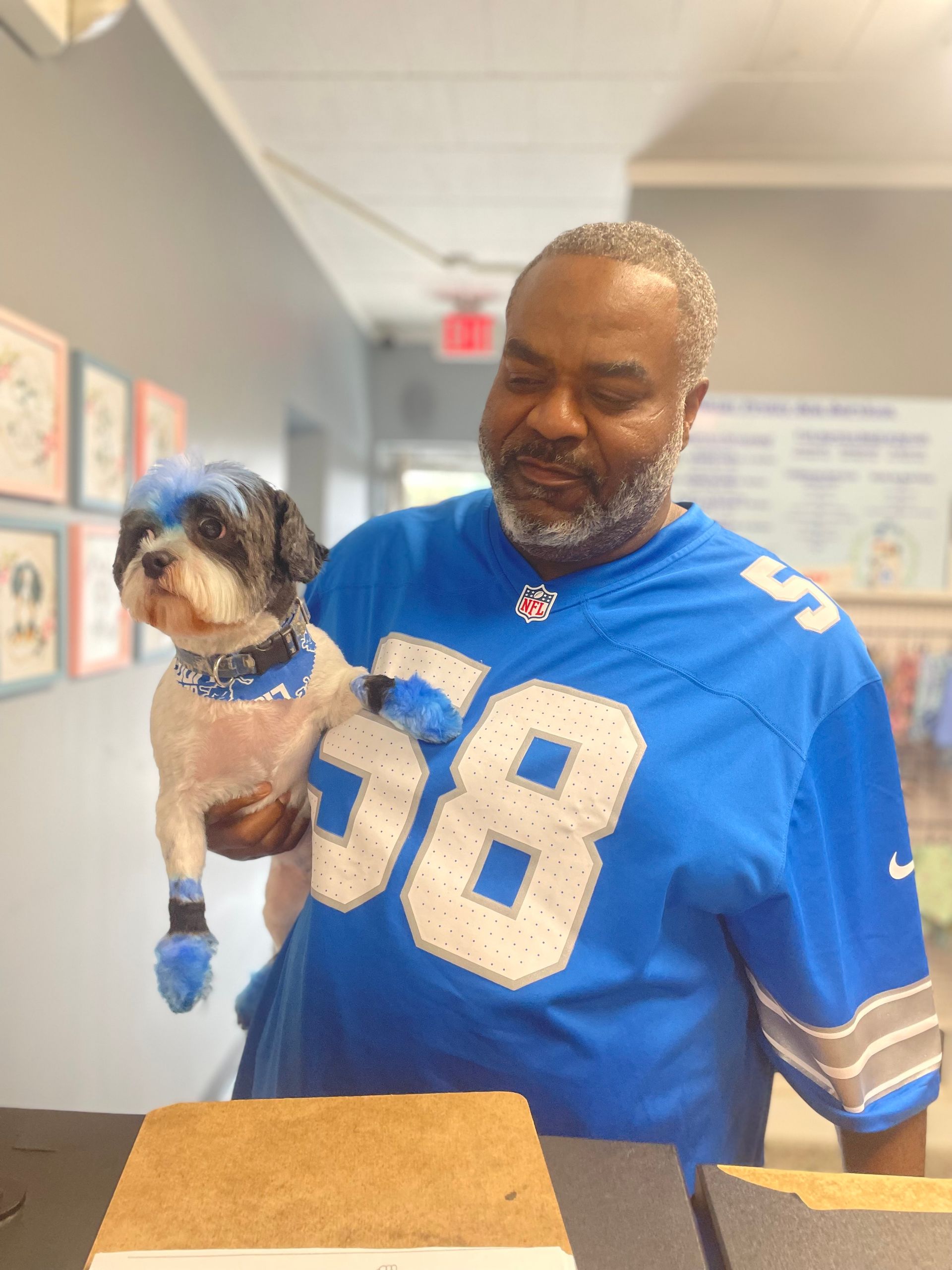 Man in Lions jersey holds dog with Detroit Lions-themed fur dye.