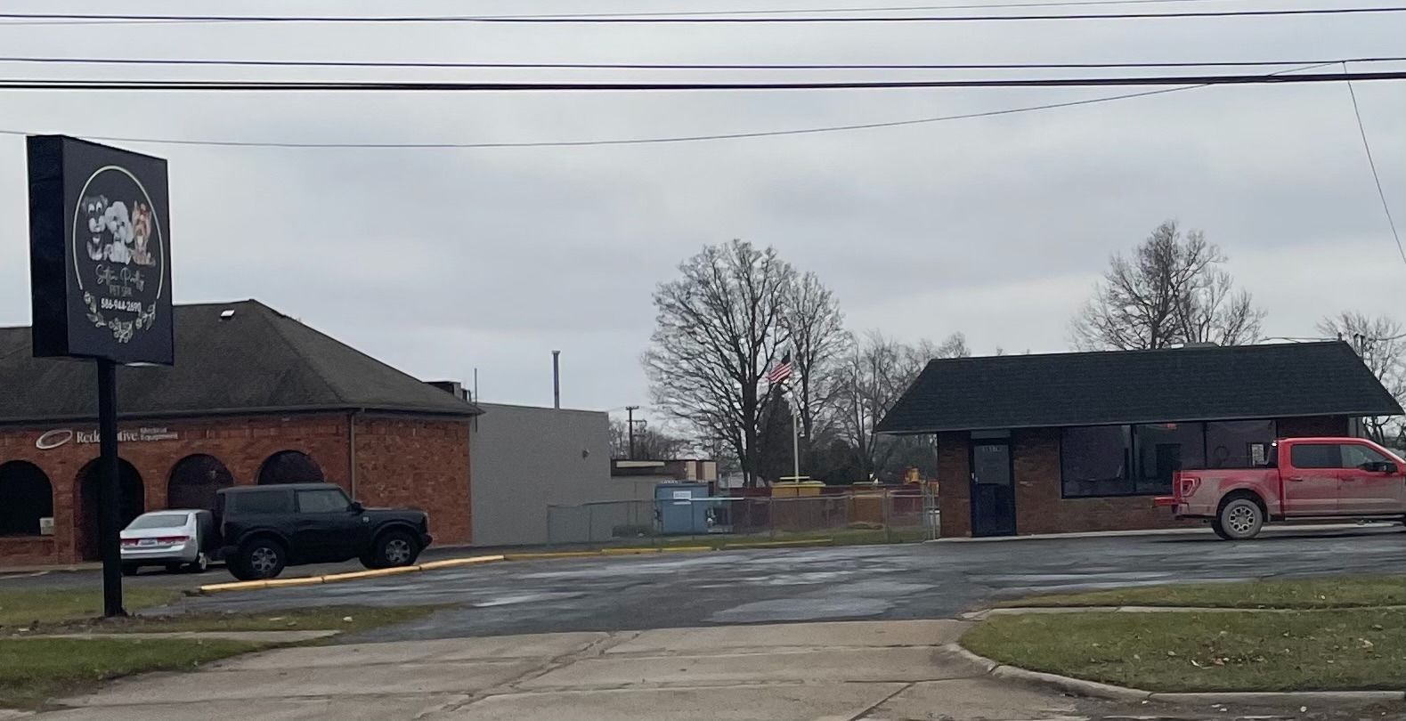 A business with a sign and two buildings with cars parked in the front. Cloudy sky.