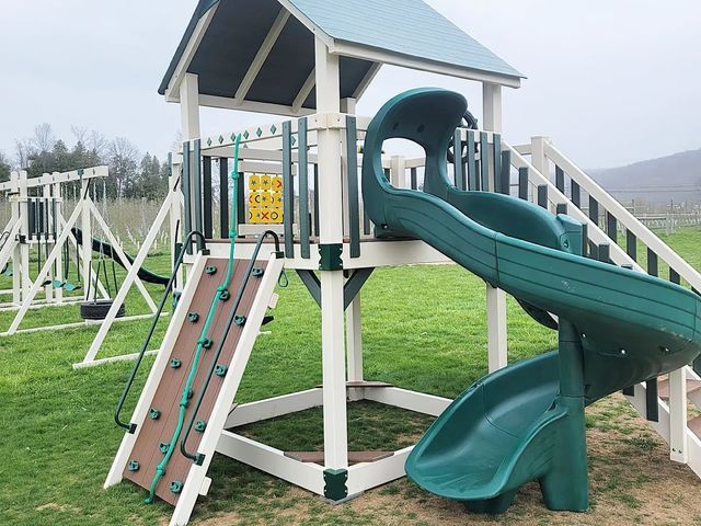 A green and white playground set with a slide and climbing wall.