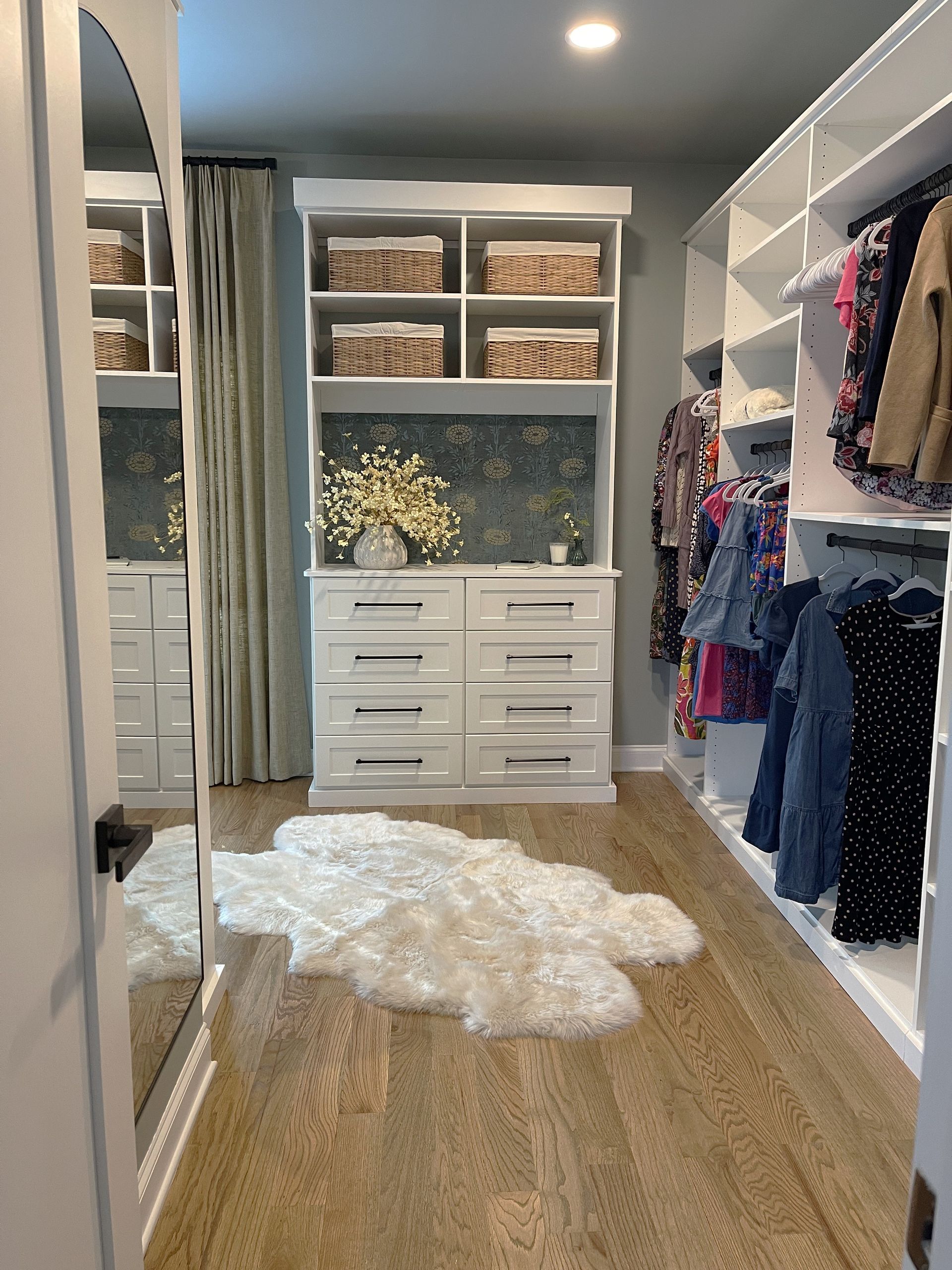 A walk in closet with lots of clothes and a rug on the floor.