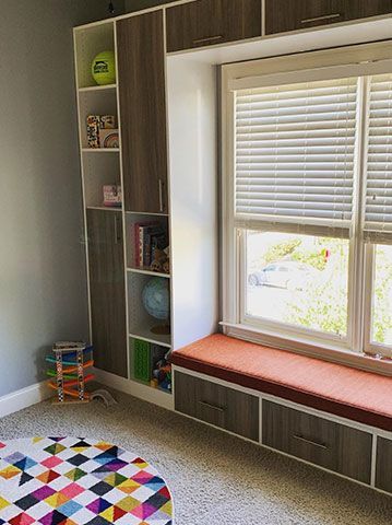 A child 's room with a window seat and shelves.