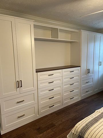 A bedroom with lots of white cabinets and drawers.