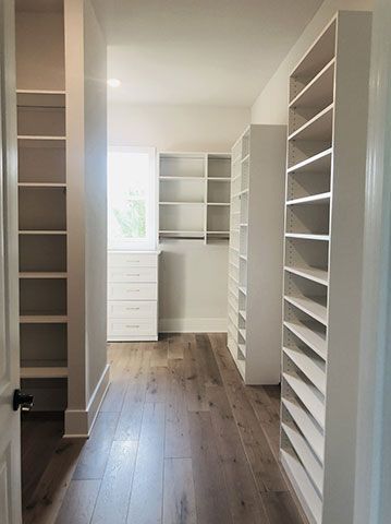 A walk in closet with hardwood floors and white shelves.