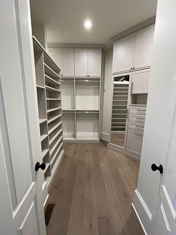 A walk in closet with hardwood floors and white cabinets.