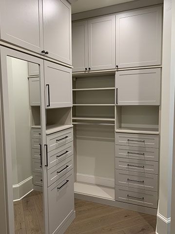 A walk in closet with white cabinets and drawers and a mirror.