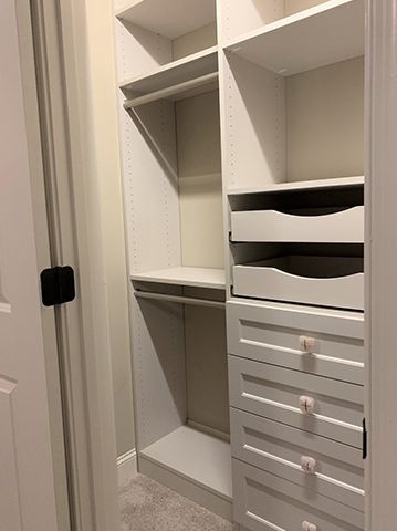 A walk in closet with white shelves and drawers.