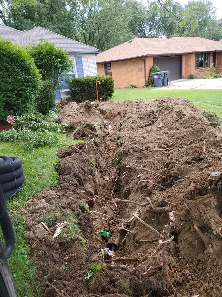 Trench dug in a front yard with dirt pile. Houses and green foliage in the background.