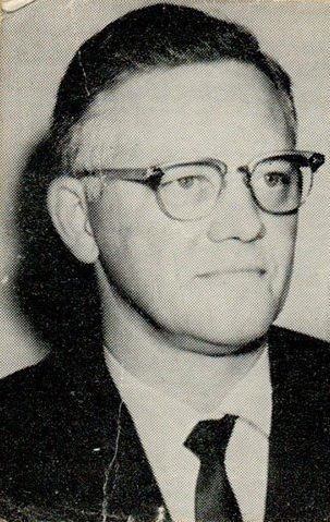 A black and white photo of a man wearing glasses and a suit and tie.
