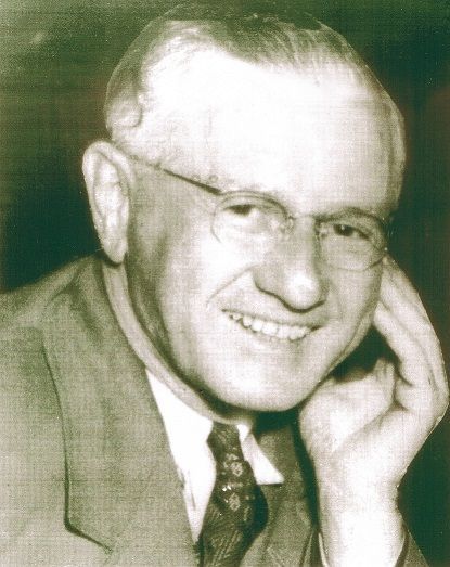 A black and white photo of a man wearing glasses and a suit.