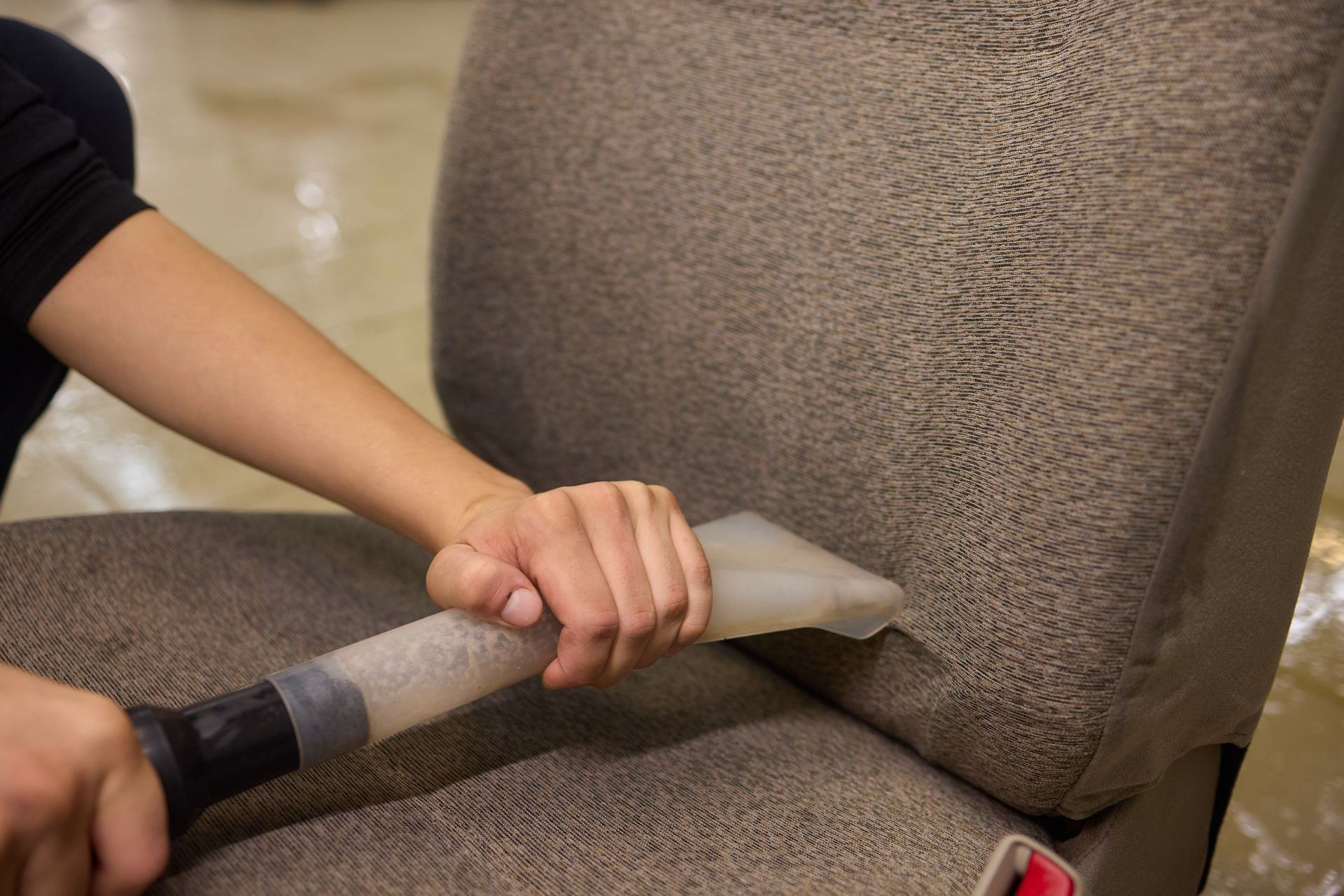 A person is cleaning a chair with a vacuum cleaner.